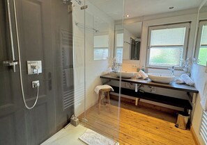 A modern bathroom with a glass shower enclosure, wooden flooring, a sink with a vessel basin, and a mirror above the vanity.