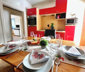 Un coin repas avec une table en bois mise pour le repas, des placards de cuisine rouges et un four à micro-ondes posé sur le plan de travail.