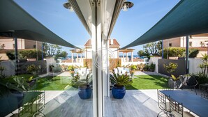 A modern outdoor patio with a glass balustrade, potted plants, and a view of a beach and buildings in the background. - Superb contemporary villa PIED DANS L'EAU - plage de l'Ayguade / with plancha (Hyères)