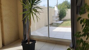 Ein Zimmer mit einer großen Schiebetür, die auf eine Terrasse mit weiß gefliestem Boden und einem kleinen Gartenbereich führt.