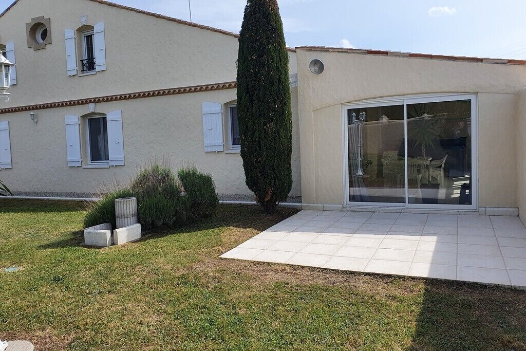A house with a tiled patio, a tall coniferous tree, and a large sliding glass door.