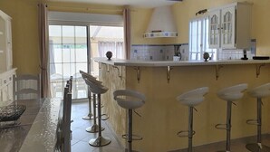 Eine Küche mit Bar, einem Esstisch mit Stühlen und Blick durch eine Glastür.