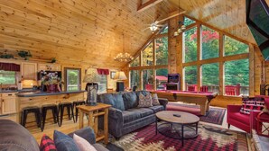 Een ruime hut met een grote eethoek, een gezellige woonkamer met een open haard en grote ramen met uitzicht op het bos.