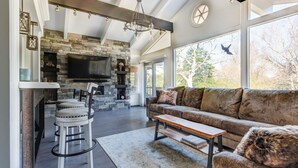 A spacious living area with a stone fireplace, a large flat-screen TV, a comfortable sofa, and a dining area with bar stools.