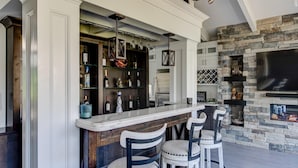 A bar area with a stone fireplace, a large TV, and a wine rack.