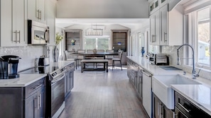 A modern kitchen with a central island, stainless steel appliances, and ample natural light from large windows. - Shinnecock Sanctuary (Southampton)