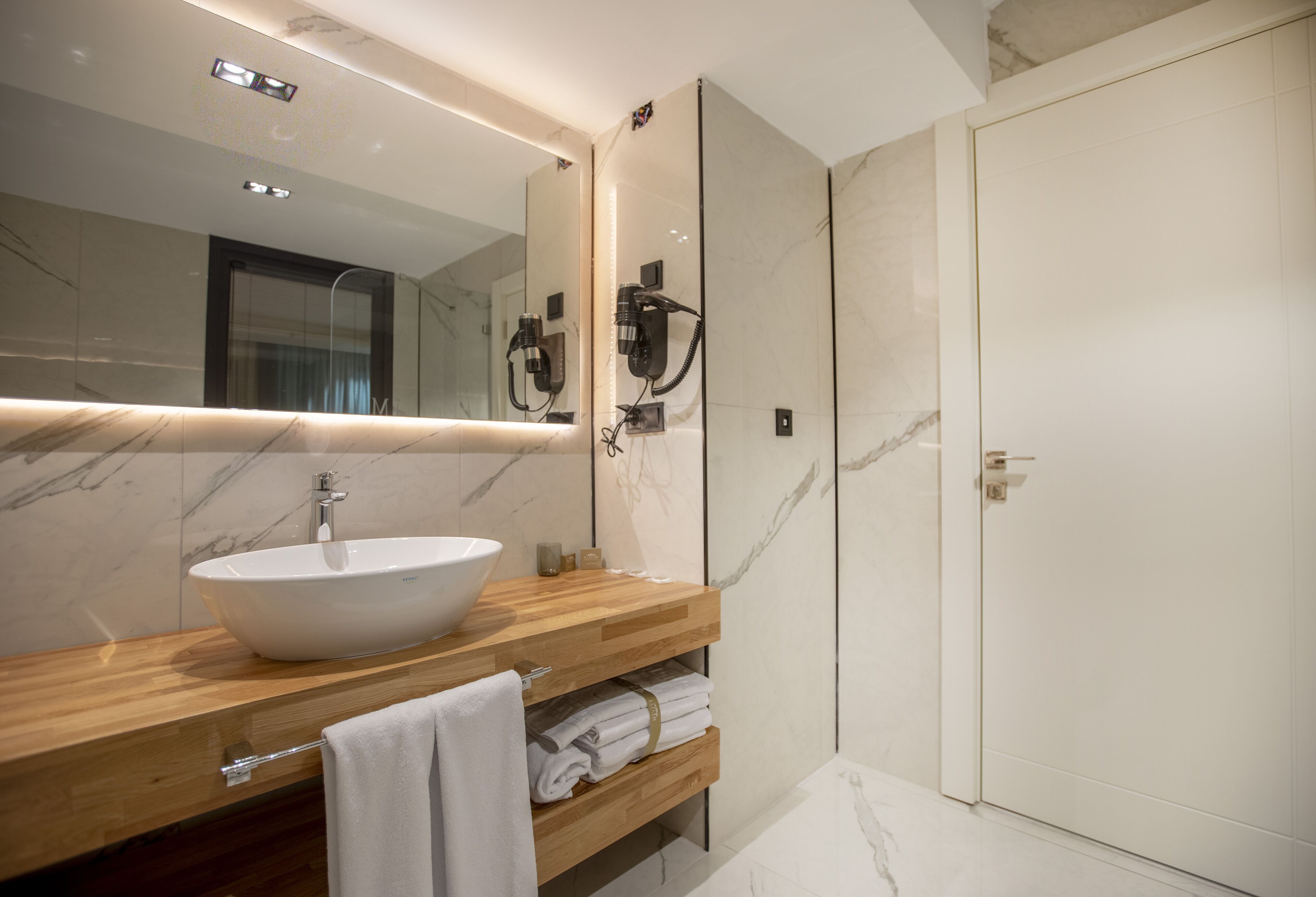 A modern bathroom with a large mirror, a white sink, and a wooden vanity.