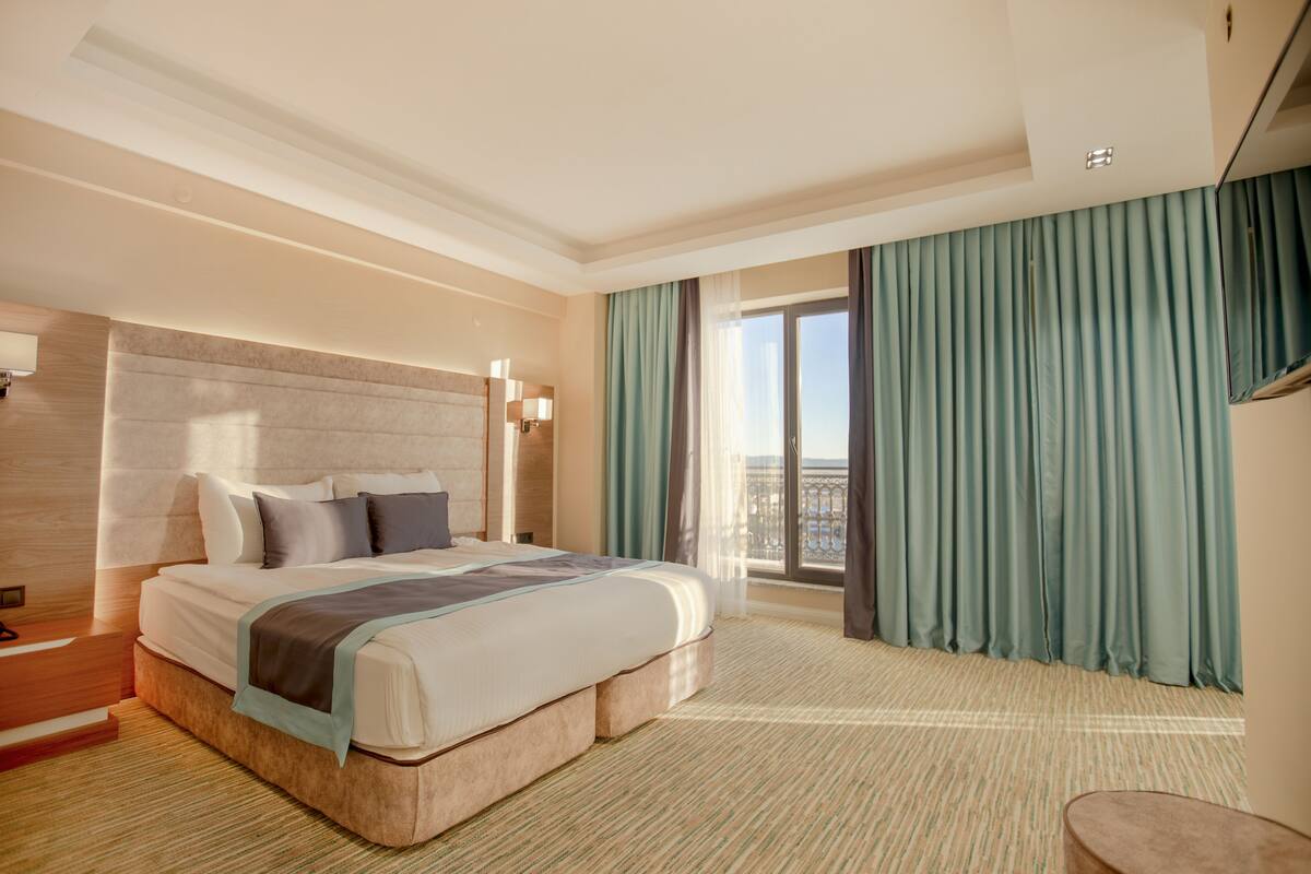 A hotel room with a large bed, a view of the city, and a balcony with curtains.