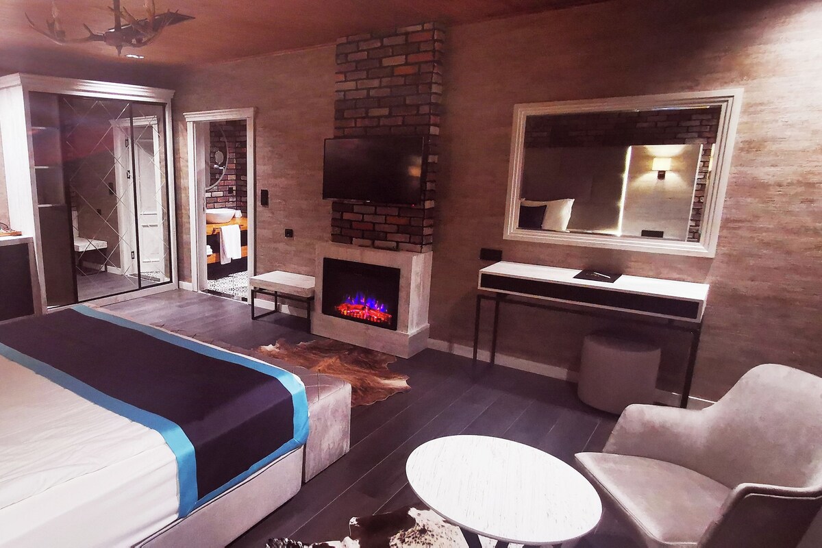 A modern bedroom with a bed, a fireplace, a desk, and a chair.