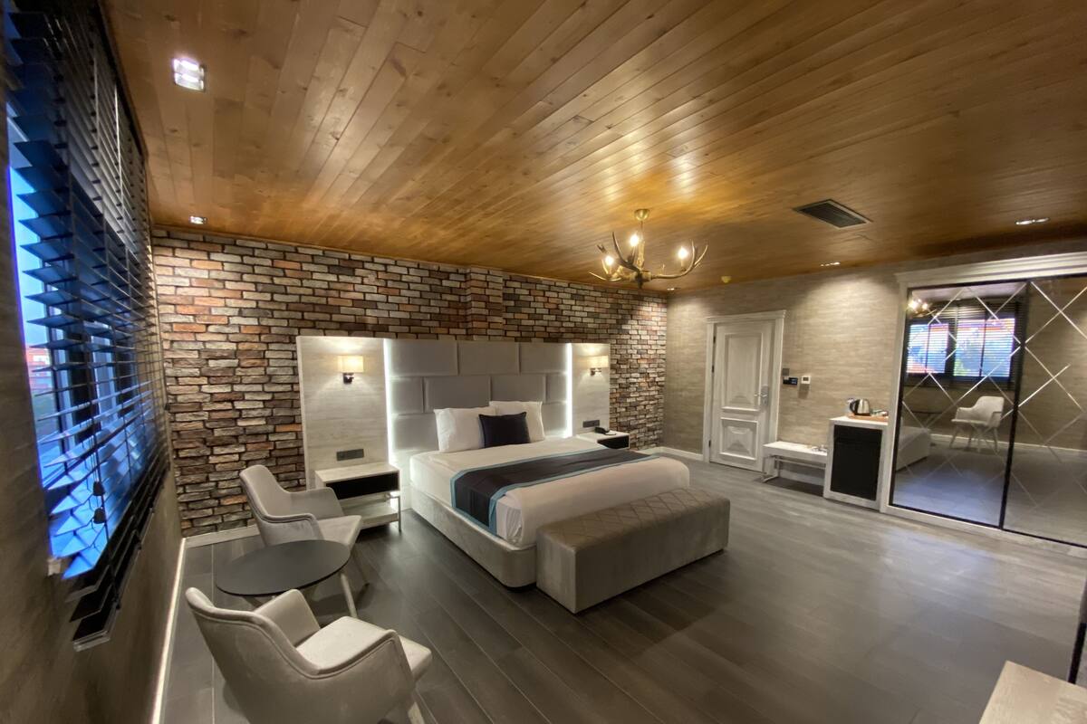 A modern bedroom with a brick accent wall, a large bed, a desk, and a chair.