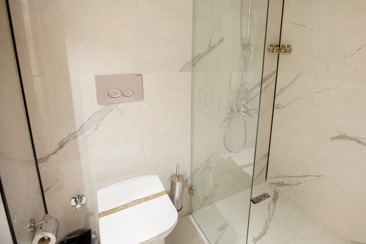 A bathroom with a glass-enclosed shower, a toilet, and a marble-tiled wall.