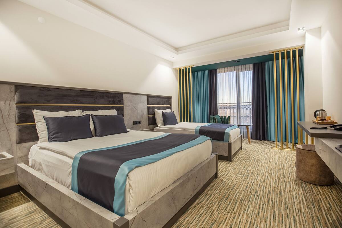 A hotel room with two beds, a desk, and a balcony with curtains.
