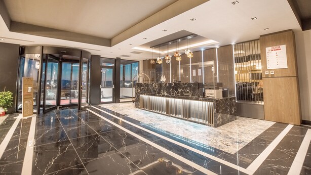 En modern hotellobby med en marmordiskinredd reception, glasdörrar som leder ut och utsikt över stadsbilden.