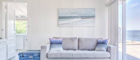 Una habitación con un sofá gris, un cuadro de una playa y un ventanal con vistas al mar.