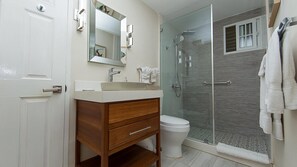 Ein Badezimmer mit einem weißen Waschbecken, einem Holz-Waschtisch, einer Duschkabine aus Glas und einer Toilette.