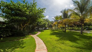 A well-maintained garden with a curved brick pathway, lush green grass, and various trees including palm trees. - Seagrapes Villa (Discovery Bay)