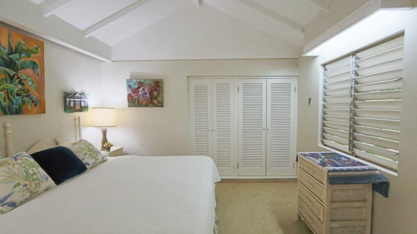 Un dormitorio con cama, cómoda, ventana con persianas, lámpara y decoración en la pared.