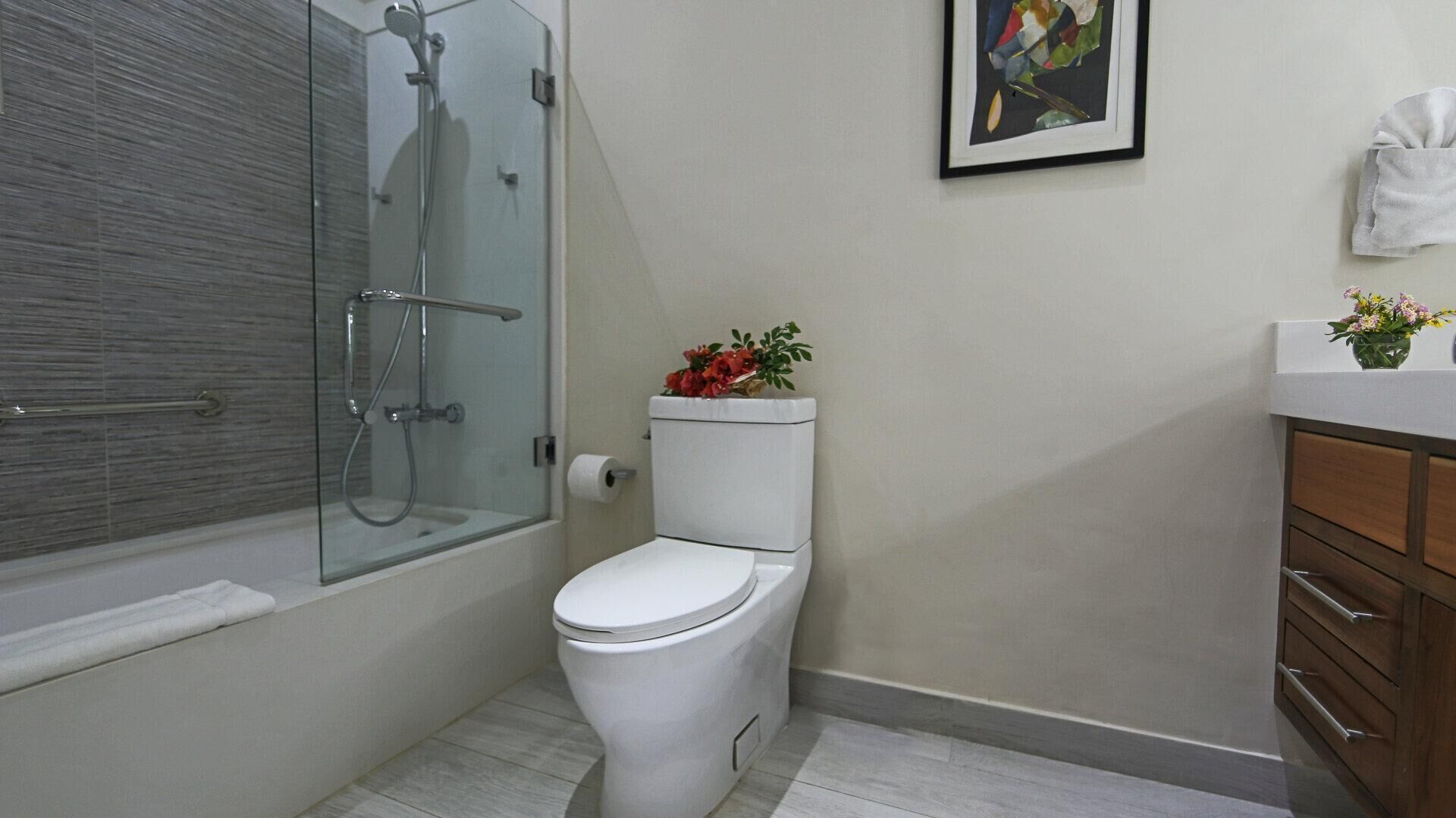 A modern bathroom with a glass-enclosed shower, a toilet with a flower arrangement, and a wooden vanity with drawers.