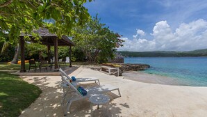 A beachside lounge with lounge chairs and a gazebo, overlooking a calm sea and a clear sky. - Seagrapes Villa (Discovery Bay)