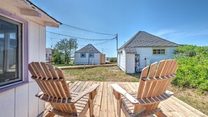 A wooden deck with two Adirondack chairs, a small white building, and a larger white building with a grey roof. - Bungalow 2 - 1br, Water View (Westhampton Beach)