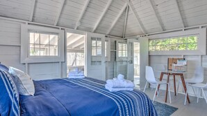 A bedroom with a bed, a desk, chairs, and a shower area. - Bungalow 2 - 1br, Water View (Westhampton Beach)