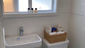 A bathroom with a white sink, a wooden box with towels, and toiletries on the window sill. - Bungalow 8 - 1br, Waterfront (Westhampton Beach)