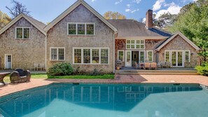 A two-story house with a swimming pool, a patio with outdoor furniture, and a brick pathway leading to the pool. - Traditional East Hampton Estate (East Hampton)