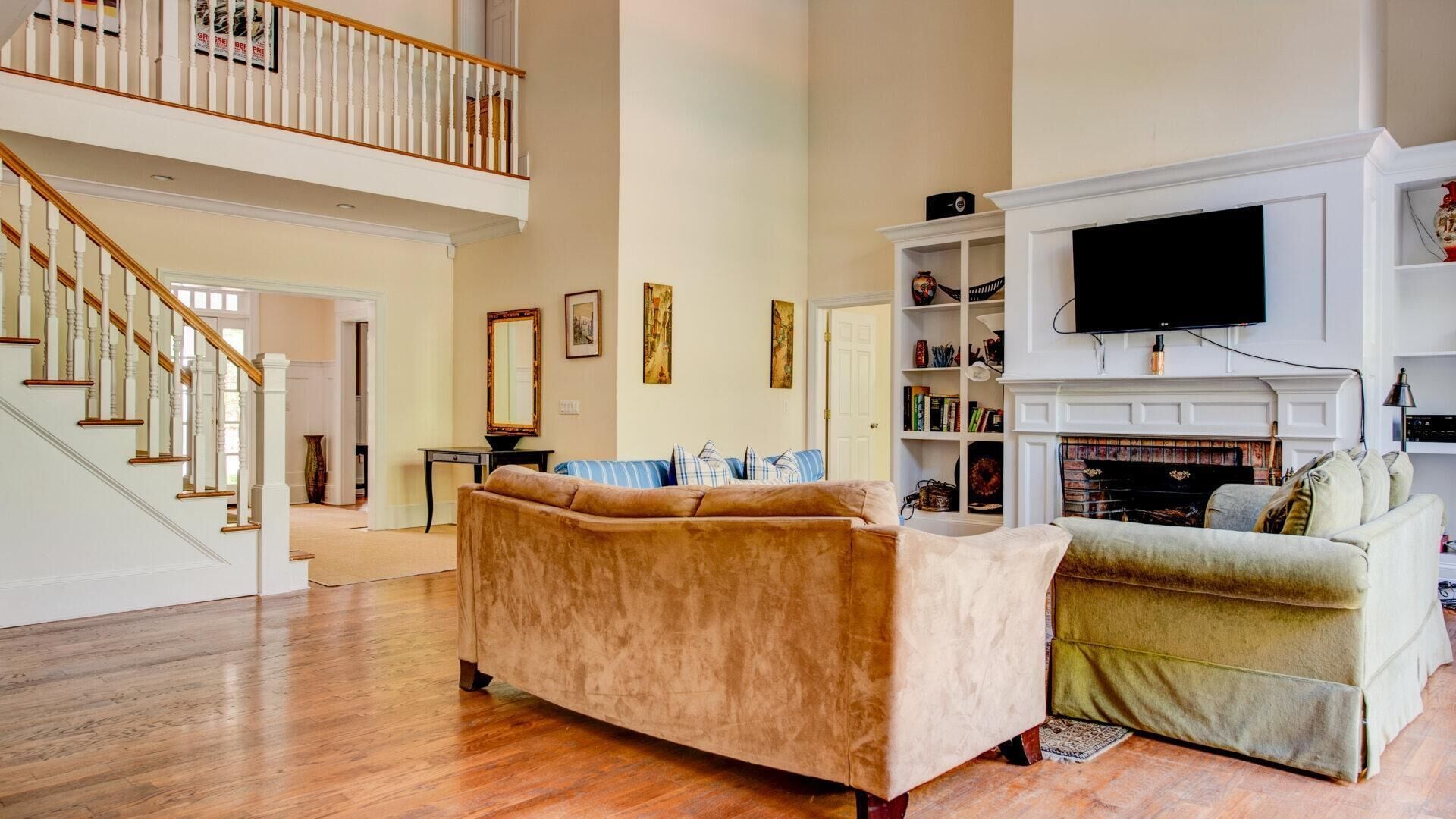 A spacious living room with a high ceiling, a fireplace, a television, and a staircase leading to an upper level.