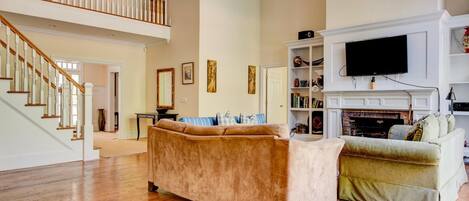 A spacious living room with a high ceiling, a fireplace, a television, and a staircase leading to an upper level.