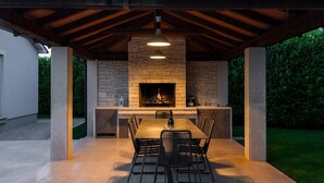 An outdoor patio with a stone fireplace, a dining table, and chairs. - Lovely Villa Gemini with a swimming pool (Visnjan)