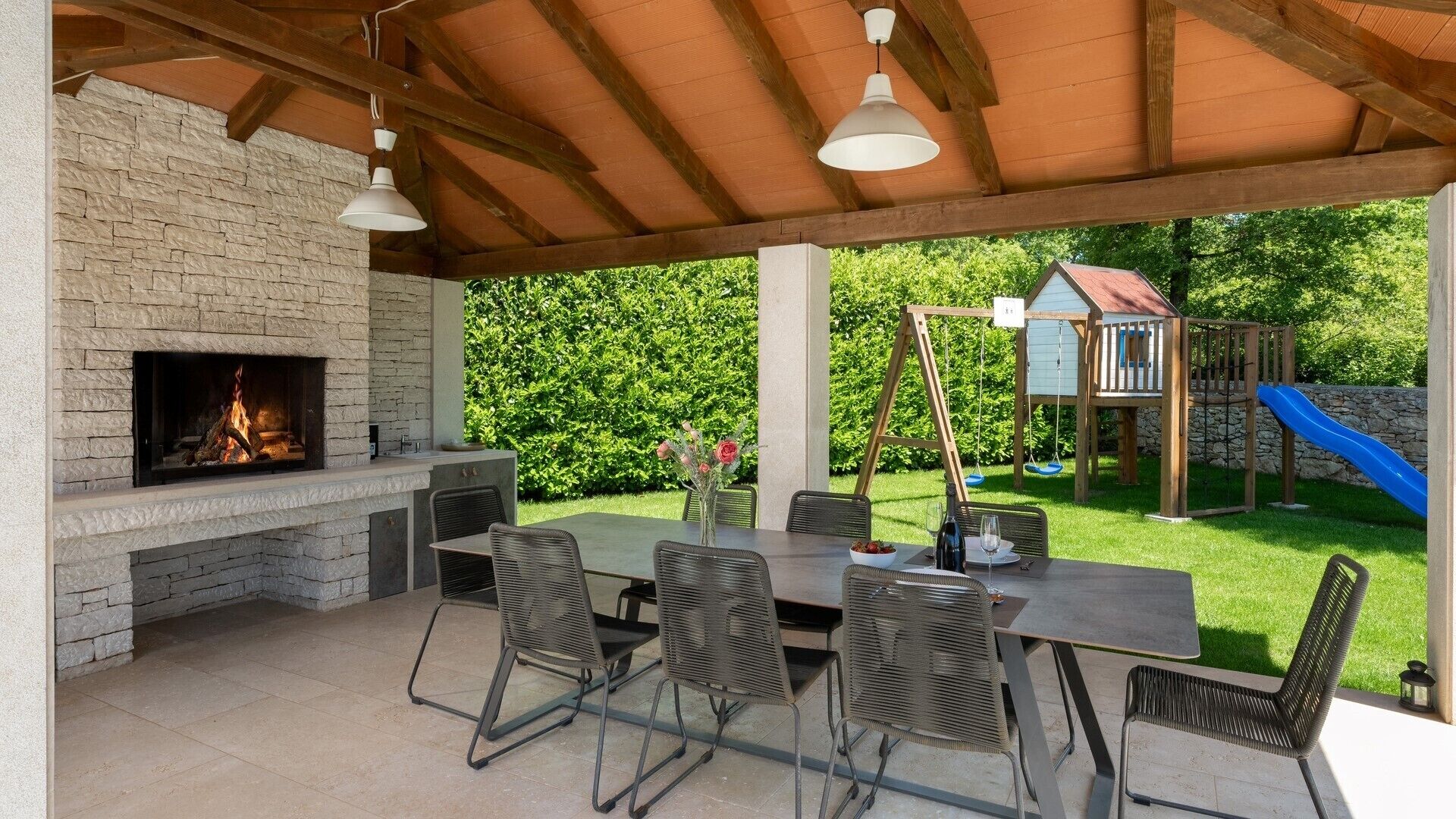 Eine Terrasse im Freien mit einem Steinkamin, einem Esstisch und Stühlen.