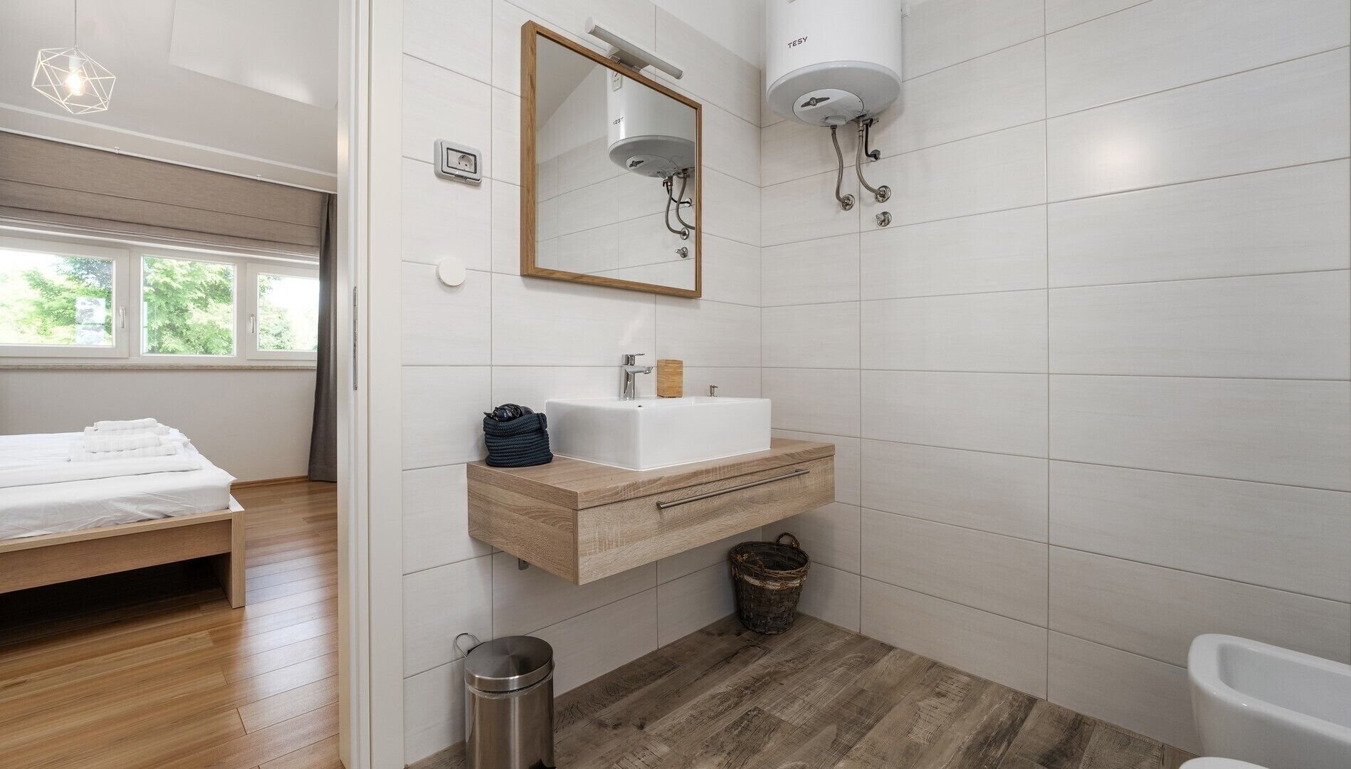 Un baño moderno con tocador de madera, un espejo grande, un lavabo blanco y una bañera.