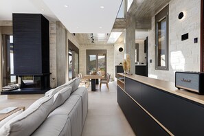 Une cuisine moderne dotée d’une cuisinière intégrée, un coin repas avec une table et des chaises en bois, et une grande fenêtre donnant sur un paysage montagneux.