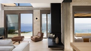 A modern living room with a large TV, comfortable seating, a fireplace, and a view of the ocean. - Stunning sea views, access to a private cove, hot tub! (Rethymno)