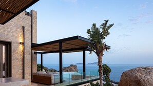 A modern outdoor living area with a glass-enclosed pool, seating, and a view of the sea. - Stunning sea views, access to a private cove, hot tub! (Rethymno)
