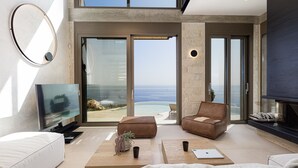 A modern living room with a large TV, comfortable seating, and a view of the ocean. - Stunning sea views, access to a private cove, hot tub! (Rethymno)