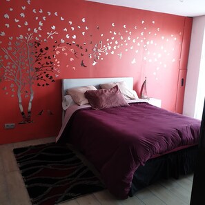 Een slaapkamer met een rode muur, een bed met een paars dekbed en een wit hoofdeinde.