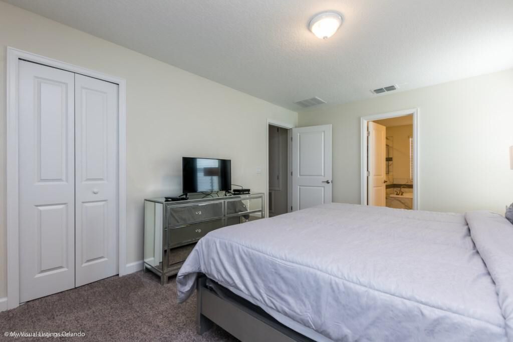Une chambre à coucher comprenant un lit, une commode, un téléviseur et une porte donnant sur une salle de bain.