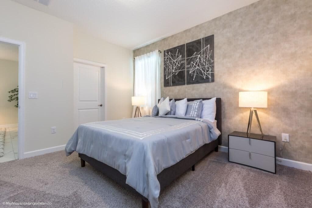 Quarto com cama, luminárias de cabeceira, mesa de cabeceira e uma obra de arte na parede.