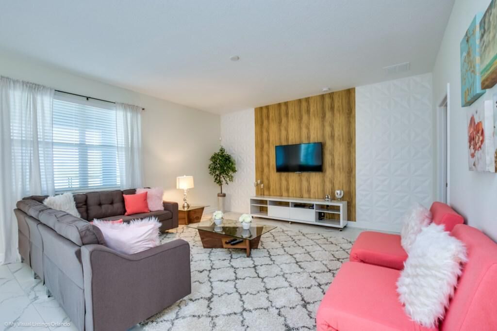 A modern living room with a grey sofa, a pink sofa, a coffee table, a TV mounted on a wooden panel, and a white patterned carpet.