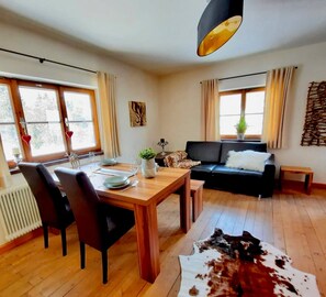 Een moderne woonkamer met een houten eettafel, een zwarte bank en een groot raam.