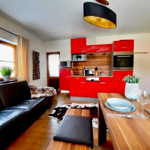 A modern kitchen with red cabinets, a black countertop, and a hanging light fixture. - Kitz Apartment 2 mit Garten Nähe Schwarzsee (Kitzbühel)