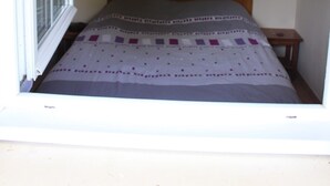 Une petite chambre à coucher avec un lit simple, deux lampes fixées au mur et une fenêtre avec des stores.