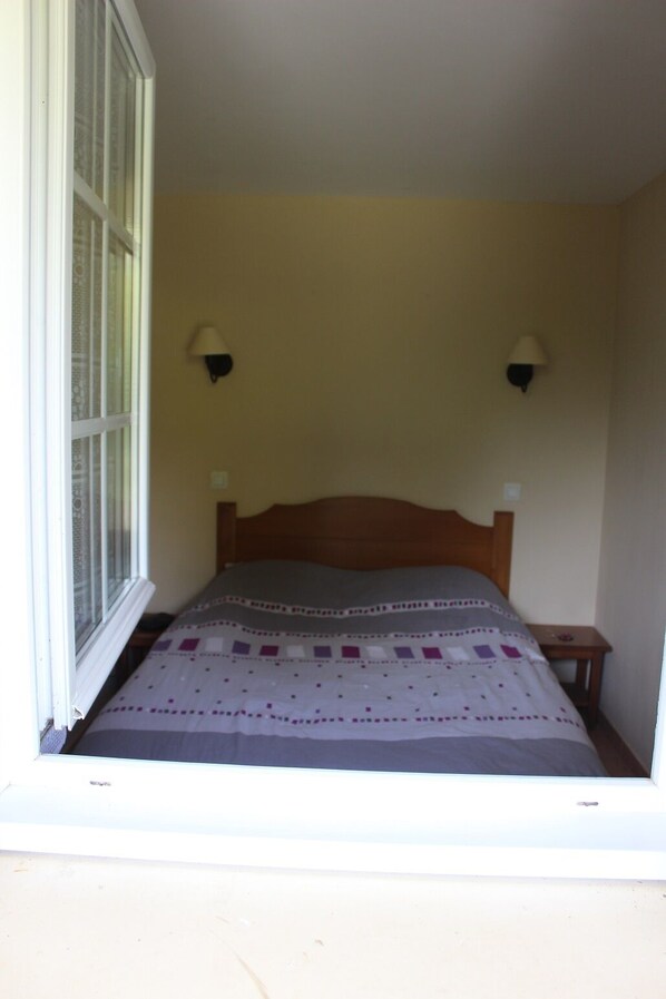 A small bedroom with a single bed, two wall-mounted lamps, and a window with blinds.