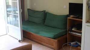 Une petite pièce avec un canapé vert, une télévision et une table.