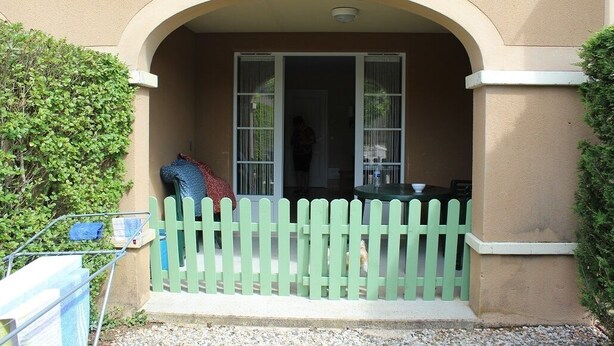 Un bâtiment avec une clôture en bois peinte en vert, un porche couvert et une fenêtre avec des rideaux.