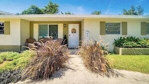 A single-story house with a front porch, a door with a sign, and a small garden with dried plants. - HEART OF MIAMI LUXURY HOME 4BR 3.5BA POOL 5MIN BEACH (Miami)