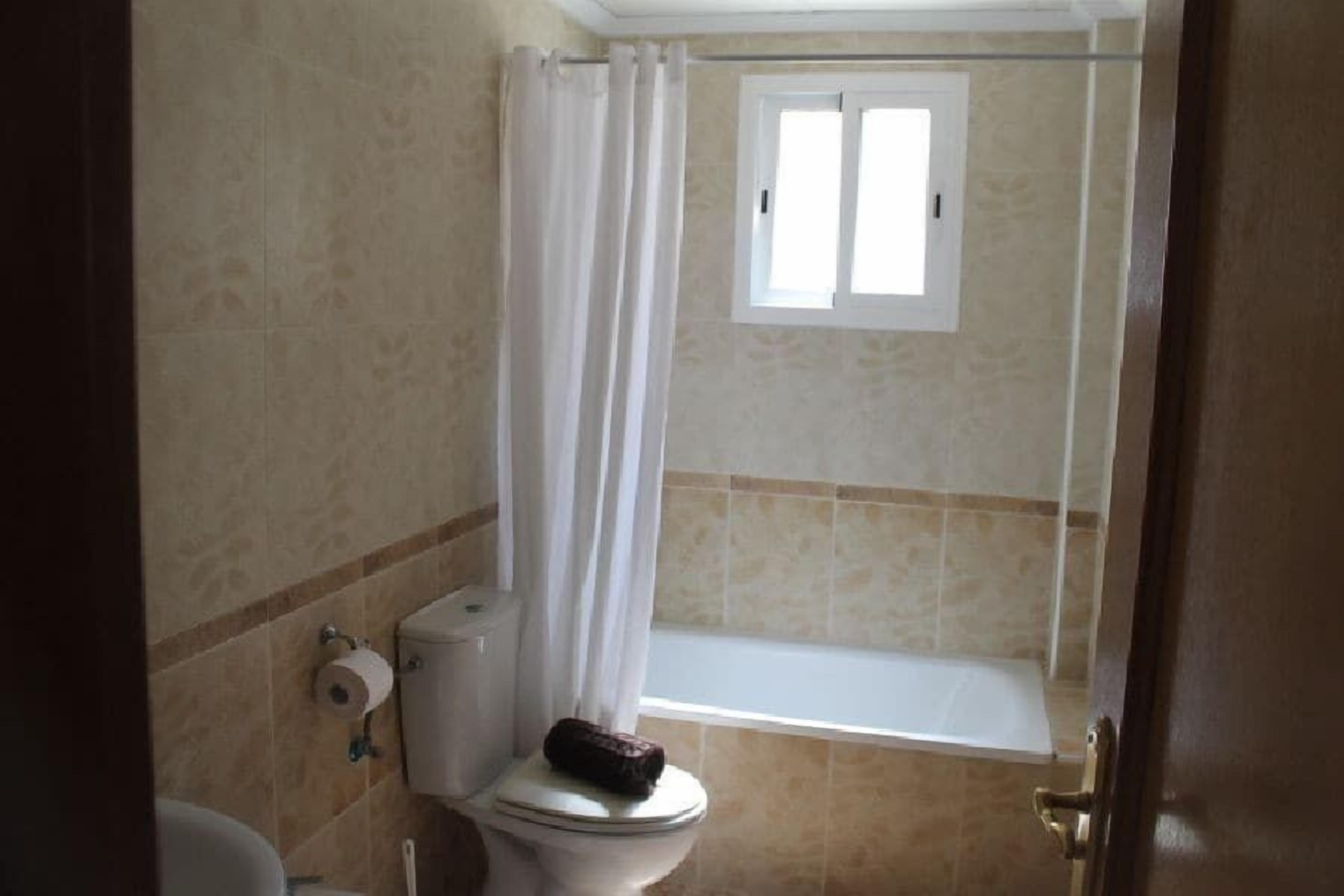 A bathroom with a toilet, a shower curtain, and a bathtub.