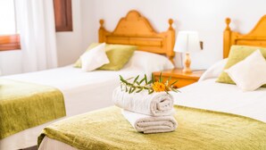 A hotel room with two beds, each with a wooden headboard, white bedding, and green throw pillows. A rolled towel with a flower arrangement is placed on the bed in the foreground. - House Sa Dalia very close to Alcudia Beach (Alcúdia)