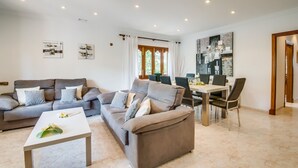 A modern living room with a grey sofa, a coffee table, and a dining area with a table and chairs. - House Sa Dalia very close to Alcudia Beach (Alcúdia)